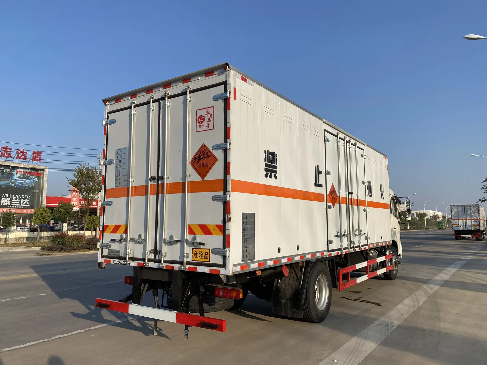 东风天锦单桥6米8爆破器材运输车 左后 45 度实拍，厢体侧门与百叶窗、「禁止烟火」大字、橙色反光带与爆炸品菱形标识，道路行驶姿态
