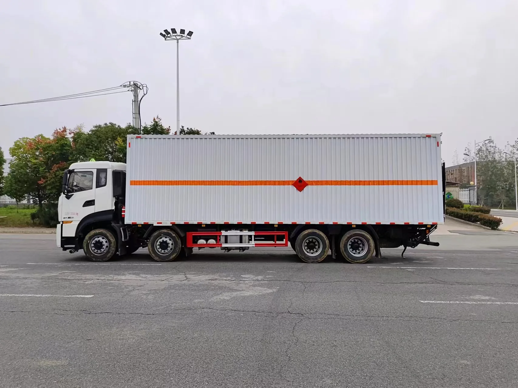 东风天龙KL前四后八危险品厢式运输车 左侧正侧面实拍：厢体橙色条带贯通 + 红色侧防护栏 + 前四后八三桥布置