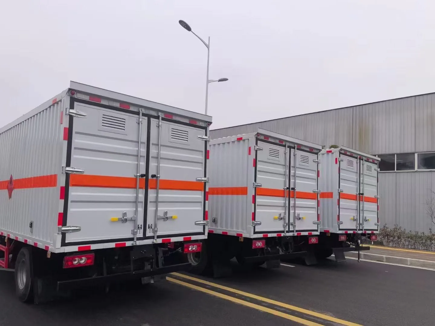  福田奥铃黄牌 5090 多介质厢式运输车，3 台车后视图，瓦楞结构厢体尾部 + 后部红色防护栏 + 橙色反光带 + 易燃气体菱形标识 + 后门金属合页 + 厂区外道路