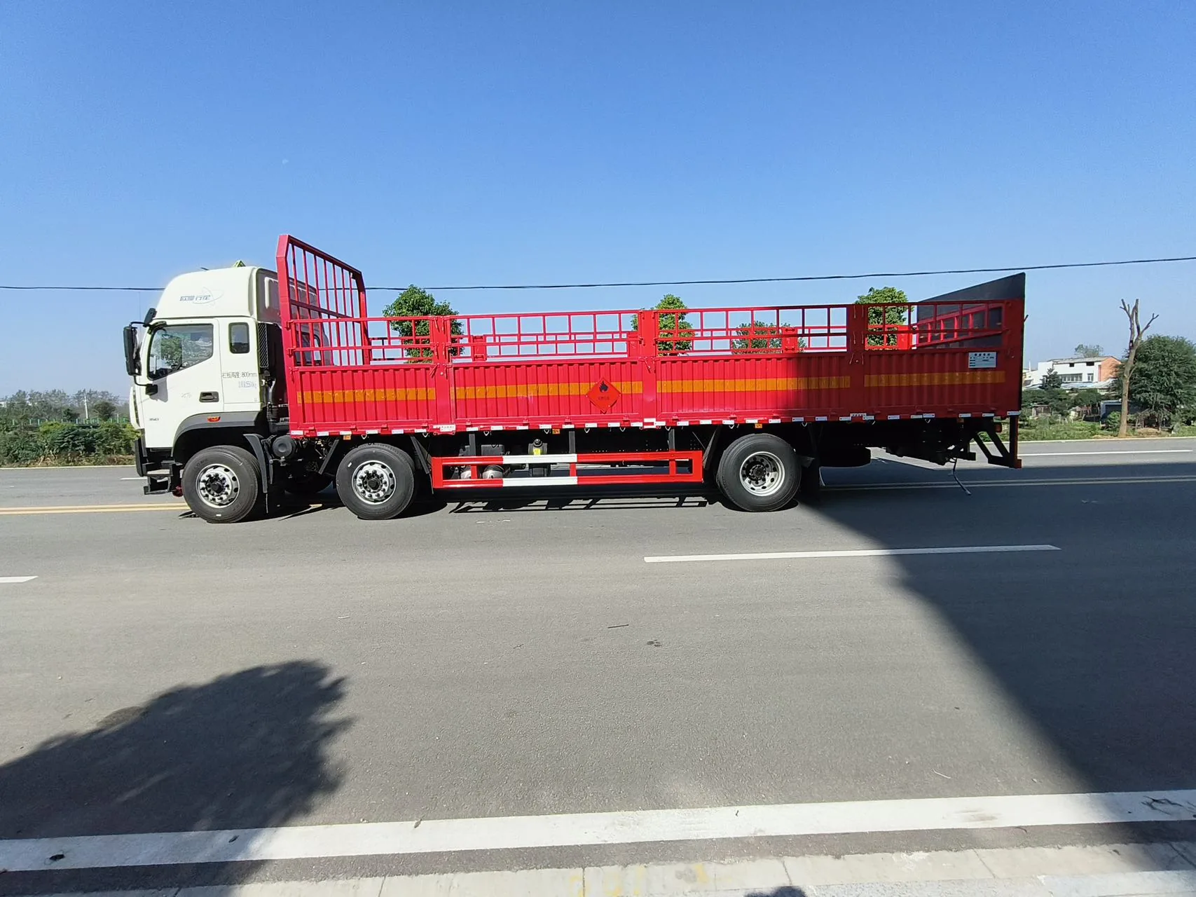 欧曼行星 9.6米仓栅式危险品运输车 右侧正侧面实拍：红色边板 + 仓栅围栏 + 菱形危险品标志 + 橙色反光带 + 侧防护栏