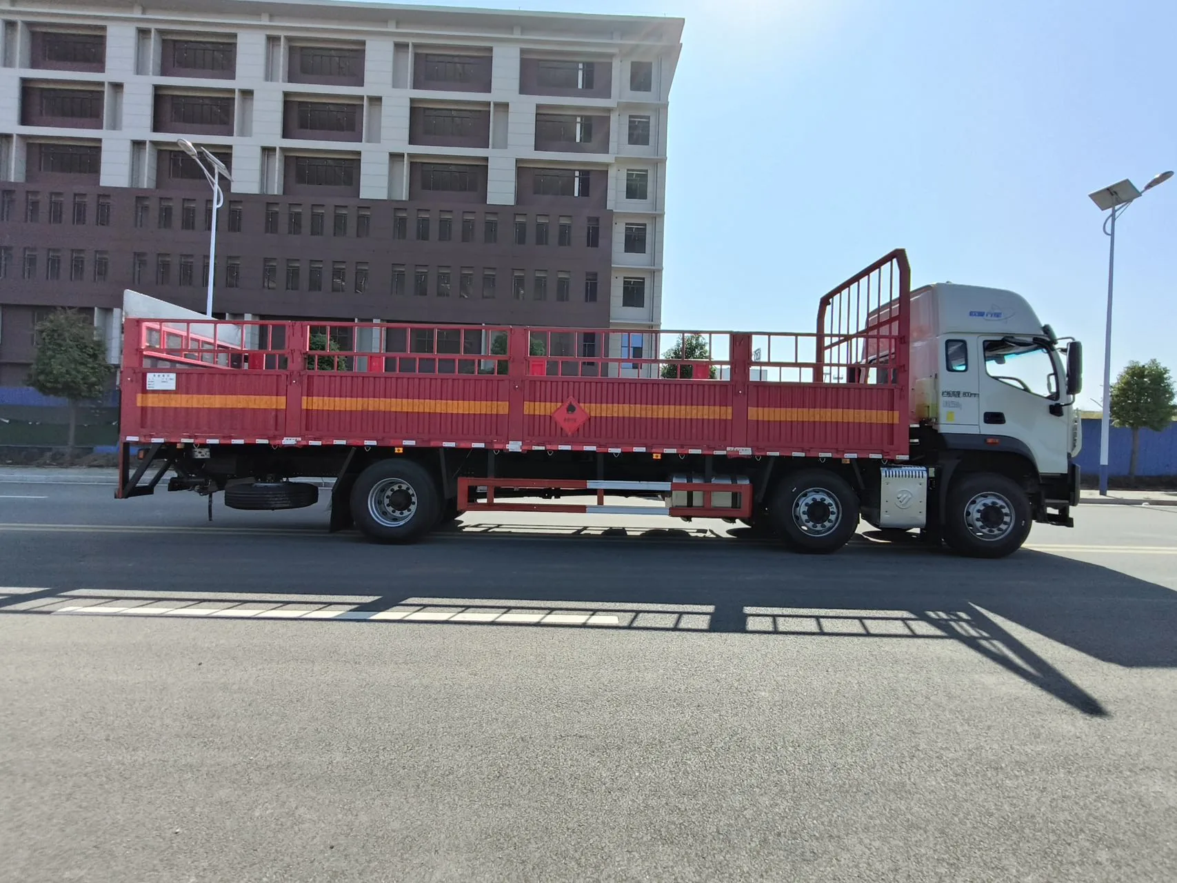 欧曼行星仓栅式危险品运输车 左后45度实拍：红色仓栅贯通 + 车厢一周反光带 + 尾部防护结构