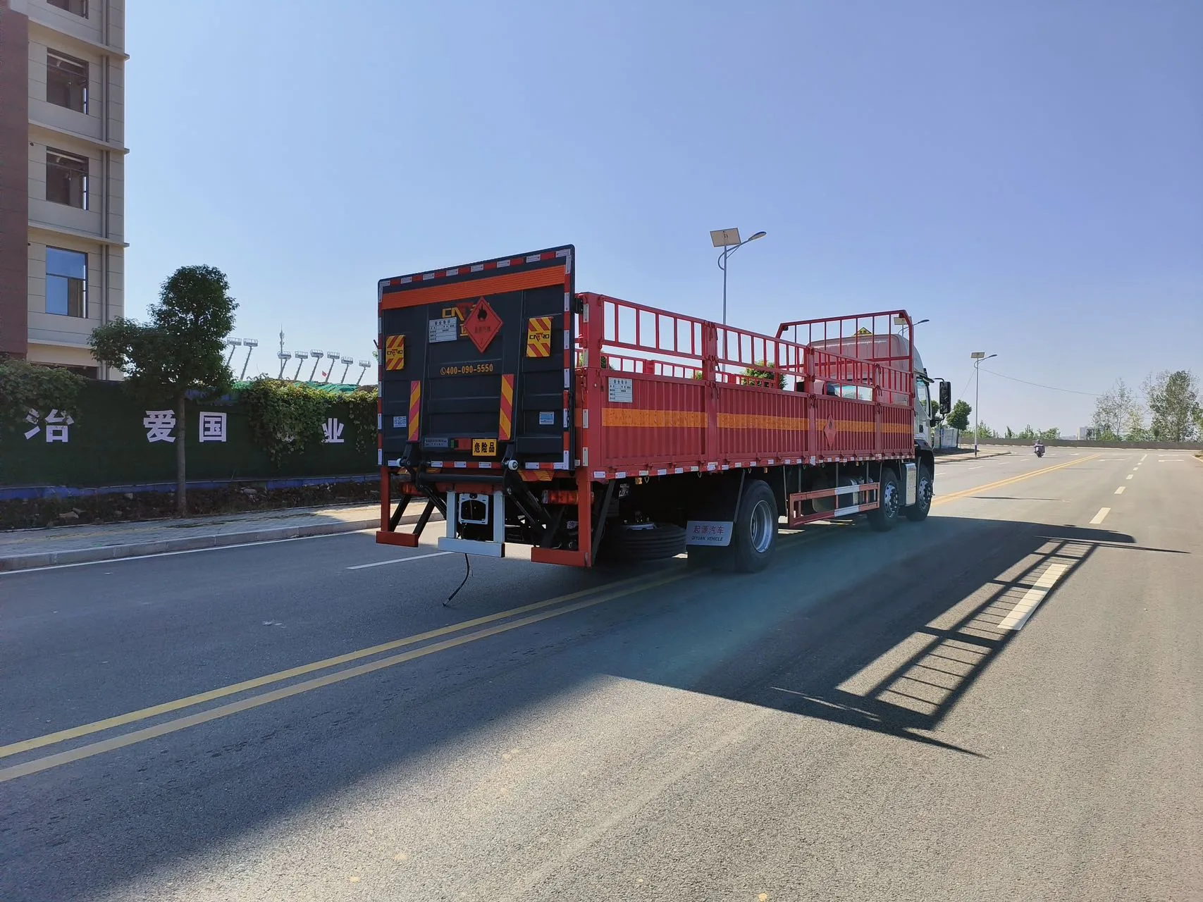 欧曼行星 9.6米仓栅式危险品运输车 右后45度实拍：尾部黑色防撞护板 + 菱形危险品标志 + 安全告示 + 橙色反光条