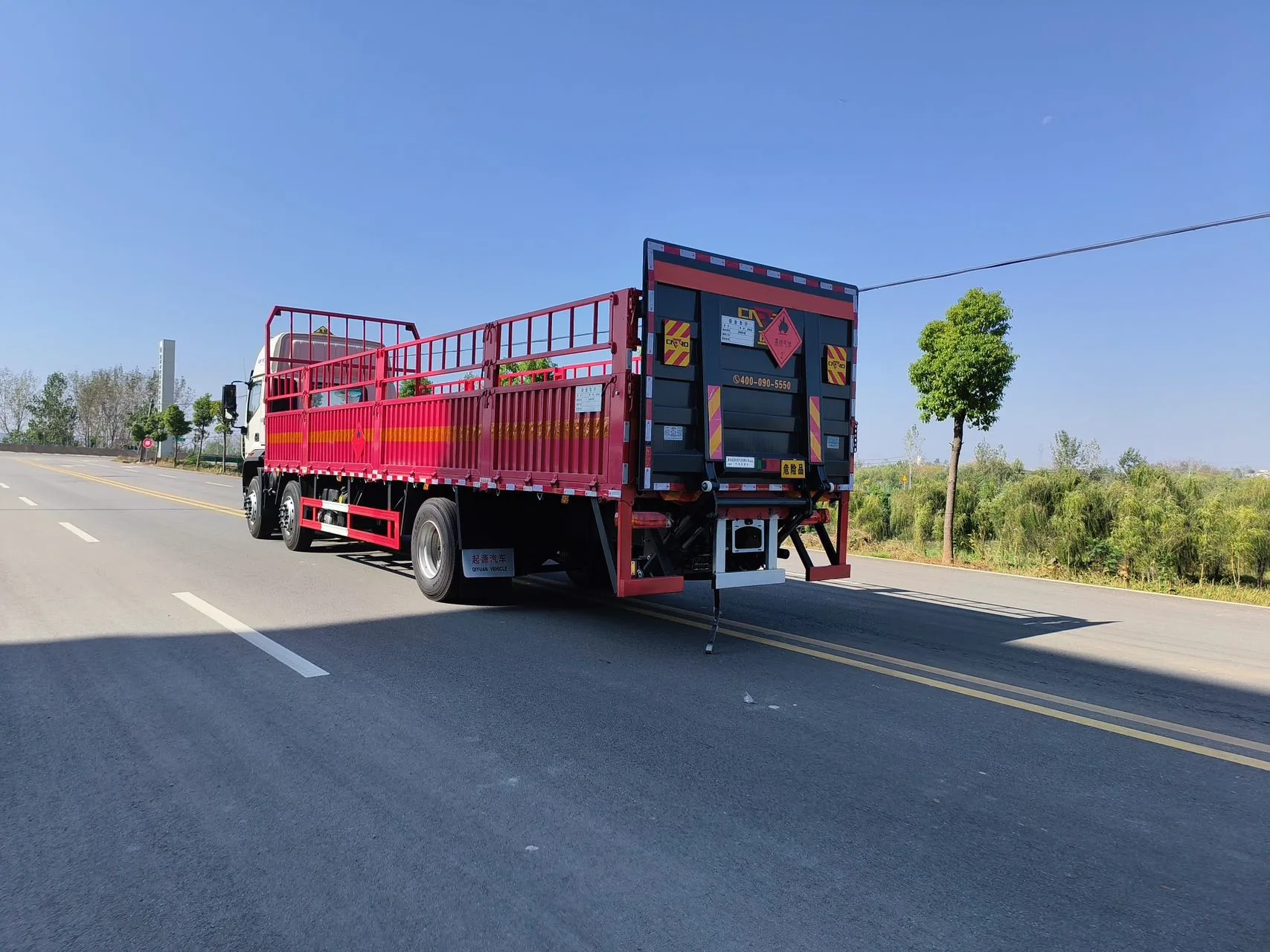 欧曼行星仓栅式危险品运输车 右后45度全景实拍：红色仓栅 + 尾部防护 + 侧防护栏 + 菱形危险品标志