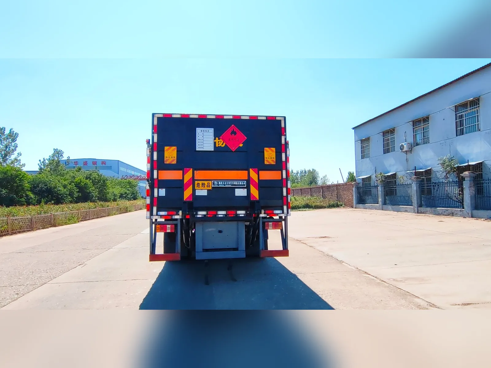 重汽豪沃单桥18吨高栏板气瓶运输车 正后尾实拍，厂区场景带活动高栏、危险品标识牌与橙色反光带