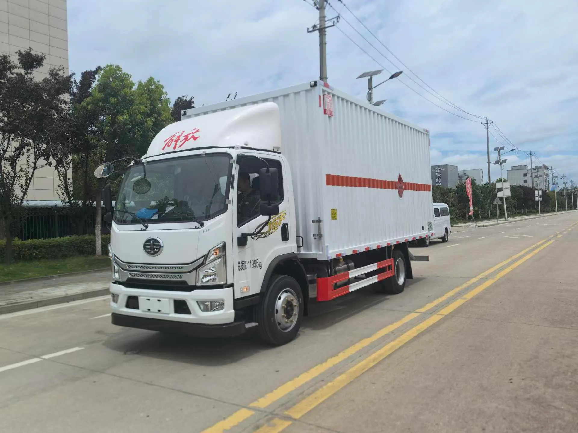 解放J6F黄牌5米2厢长危化品厢式运输车 白色厢体整车左前45度实拍：白色宽体驾驶室 + 白色瓦楞厢体 + 红色反光腰线 + 黄色菱形腐蚀品标识 + 总质量11995kg