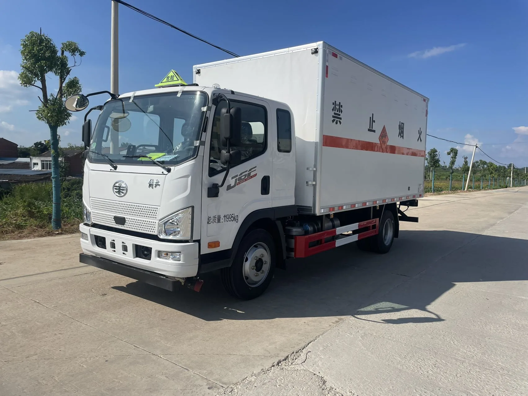 解放J6F黄牌5米2厢长危化品厢式运输车 白色厢体整车左前45度实拍：解放鹰标 + 白色宽体驾驶室 + 白色瓦楞厢体 + 红色反光腰线 + 黄色菱形禁止烟火标识 + 总质量11905kg