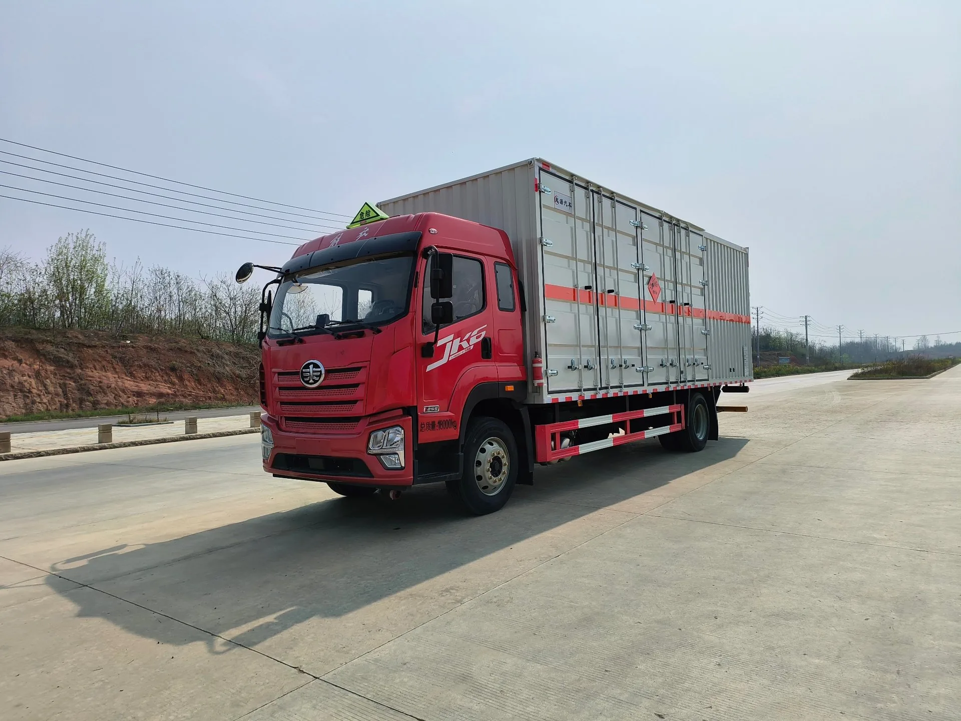 解放JK6危险品厢式运输车 白色厢体整车右前45度实拍：JK6红头驾驶室+白色复合厢体+黄色危险品菱形标+红色反光腰线，户外公路背景