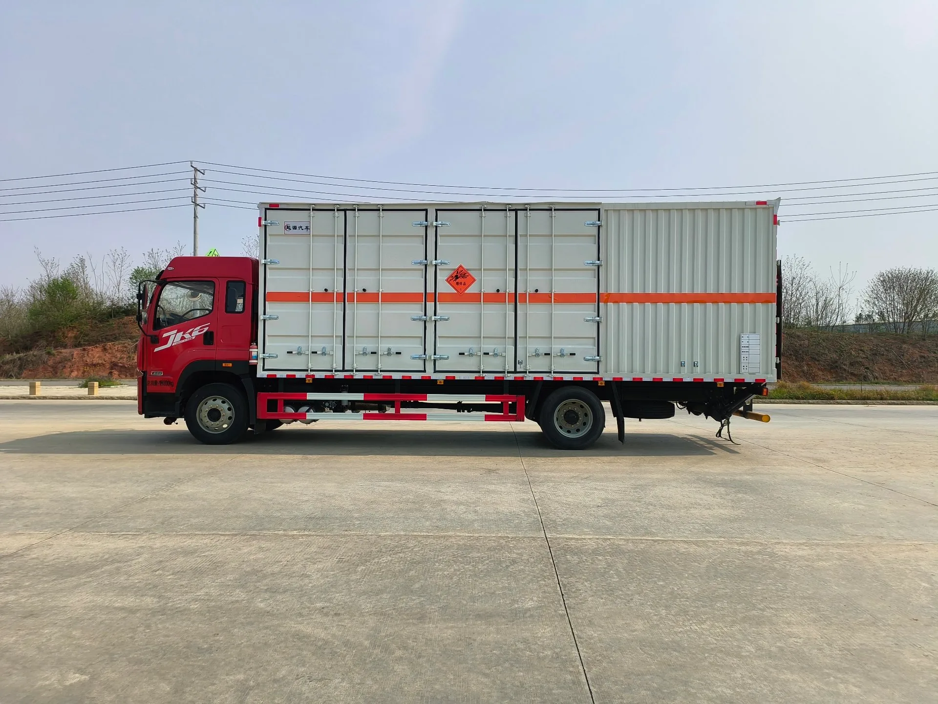解放JK6危险品厢式运输车 白色厢体整车正侧面实拍：JK6红头驾驶室+白色复合厢体+黄色危险品菱形标+红色反光腰线，户外公路背景