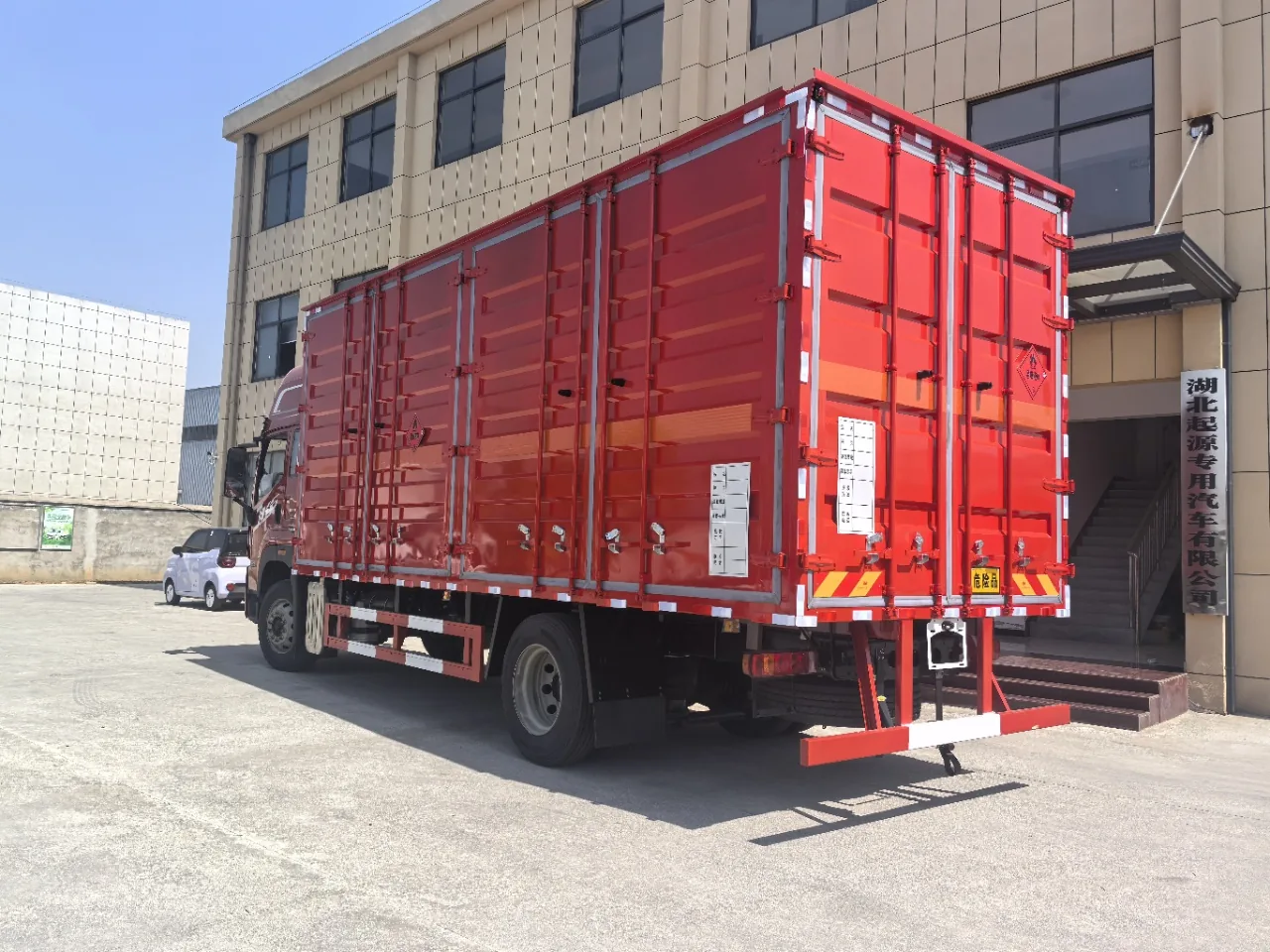 解放JK6危险品厢式运输车 红色厢体右后45度实拍：JK6红头驾驶室+红色复合厢体+黄色危险品菱形标，背景为湖北起源专用汽车有限公司厂房