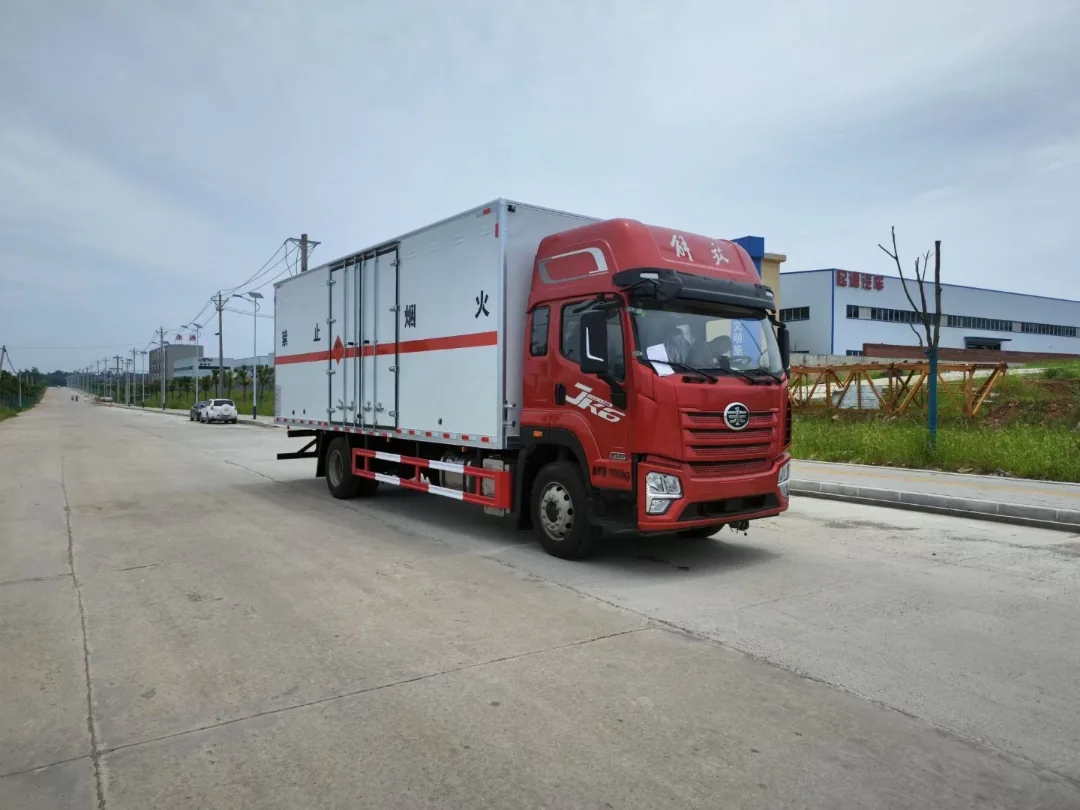 解放JK6危险品厢式运输车 白色厢体整车左前45度实拍：JK6红头驾驶室+白色复合厢体+运烟火标识+红色反光腰线，户外厂区旁