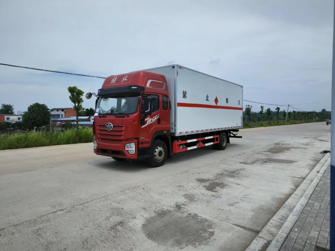 解放JK6危险品厢式运输车 白色厢体整车左前侧实拍：JK6红头驾驶室+白色复合厢体+禁止烟火标识+红色反光腰线，户外厂区