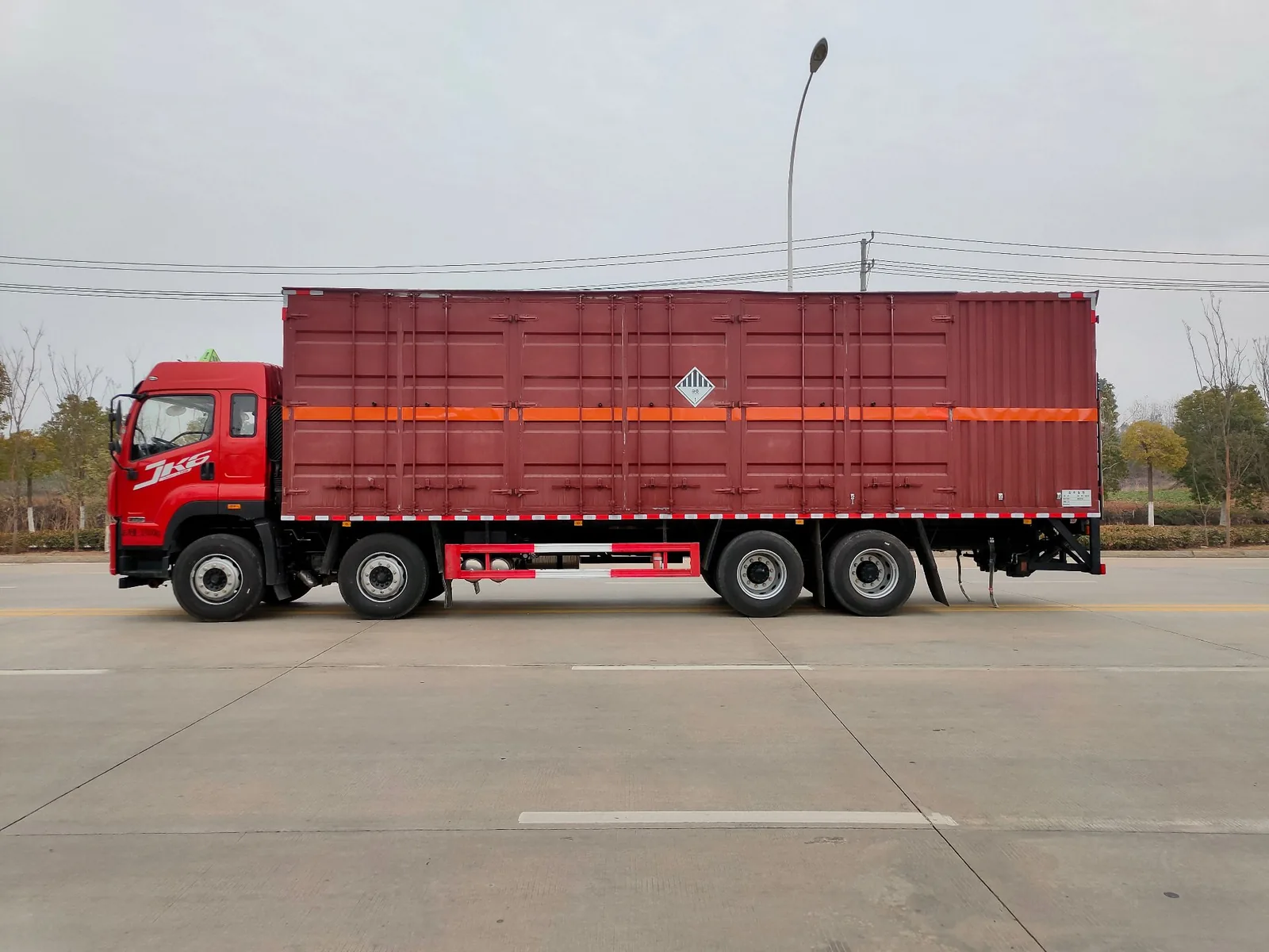 解放JK6前四后八杂项危废厢式运输车 左侧正侧面实拍：红色瓦楞厢体（9.6米长）+ 橙色反光大带 + 杂项危险物品菱形标志 + JK6半高顶驾驶室 + 空气悬架4气囊
