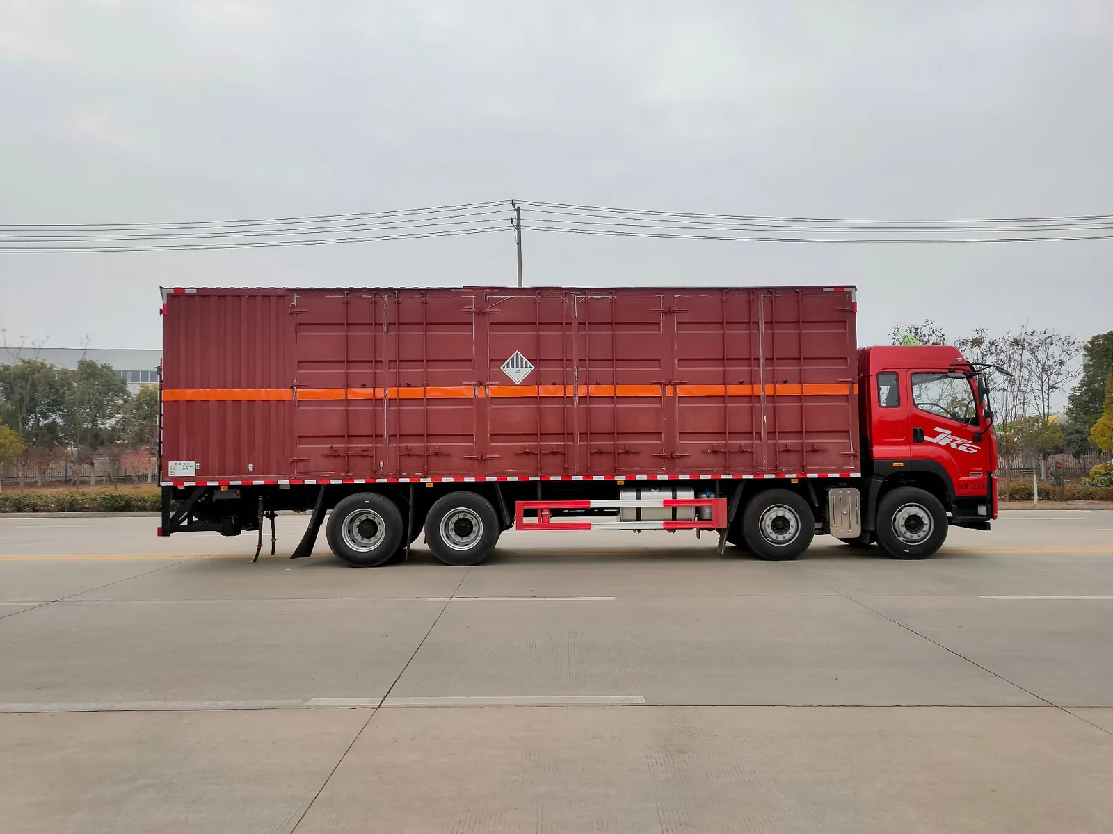 解放JK6 32吨双公告危险品厢式运输车 右侧正侧面实拍：红色瓦楞厢体 + 橙色反光带 + 杂项危险品菱形牌 + 400L铝合金油箱 + 295/80R22.5轮胎 + 前四后八轴型