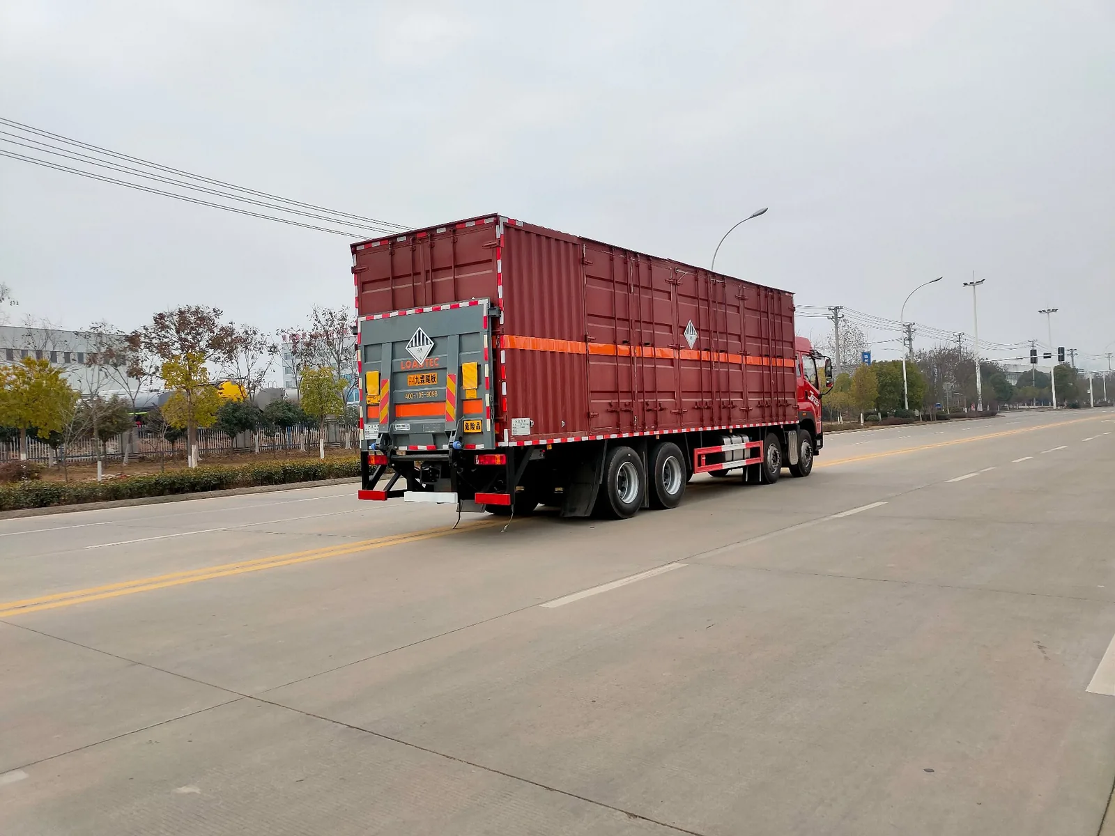 解放JK6杂项危废3类易燃液体厢式运输车 左后45度实拍：后对开门厢体 + 橙色反光带 + 危险品标志牌 + 尾部防护 + U型后处理器