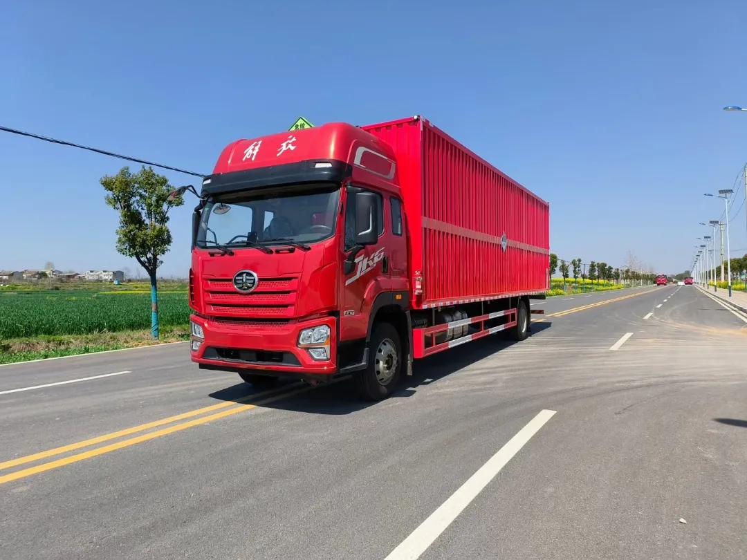 解放JK6单桥危险品厢式运输车 右前45度行驶实拍：红色瓦楞厢体 + 橙色反光带 + 杂项危险物品菱形标，乡村公路背景