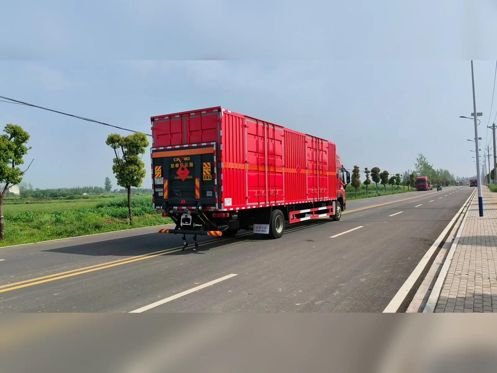 解放JK6单桥危险品厢式运输车 右后45度行驶实拍：尾部液压升降尾板（收起状态）+ 红色瓦楞厢体 + 橙色反光带，公路行驶