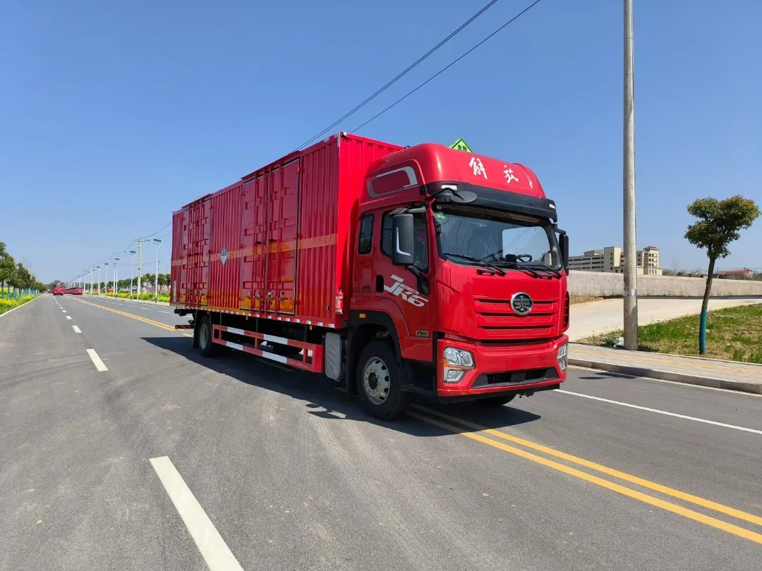 解放JK6单桥危险品厢式运输车 左前45度行驶实拍：JK6高顶全浮红色驾驶室 + 9.6米红色瓦楞厢体 + 橙色反光腰线 + 杂项危险物品菱形标志 + 危险品顶灯