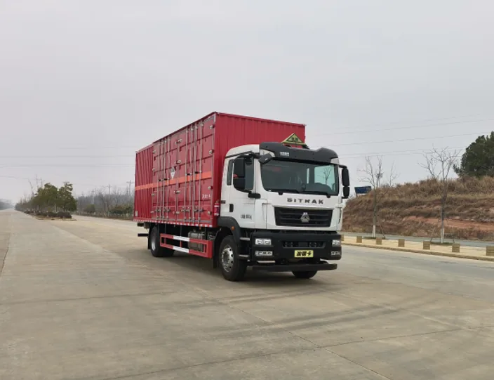 众德牌 重汽汕德卡 9.6 米危险品厢式运输车，右前 45 度视角，白色驾驶室（汕德卡标志 + 绿色危险品三角顶灯）+ 红色厢体（瓦楞结构+橙色反光带+菱形告示牌）+ 红色防护栏 + 黄色车牌「油特字」，厂区外公路，背景为土坡和绿植