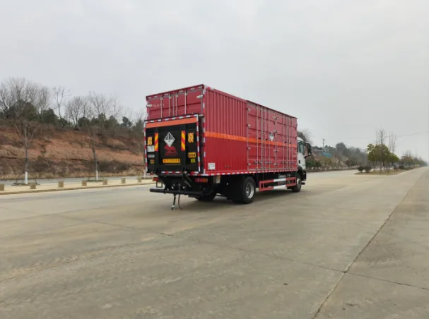 众德牌 重汽汕德卡 9.6 米危险品厢式运输车，后左 45 度视角，红色厢体尾部（瓦楞结构）+ 菱形告示牌（爆炸品/危险品标识） + 危险品标牌（介质标识+UN 编号）+ 红色防护栏 + 黄色车牌，厂区外公路