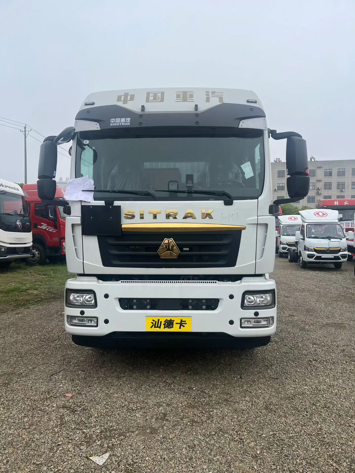 众德牌 重汽汕德卡 G5S 9.6 米危险品厢式运输车，正前视角，SITRAK 标志在驾驶室前面正面最清晰（中国重汽顶标 + 黄色车牌「汕德卡」），白色驾驶室，G5S 高配细节（高位保险杠、雾灯、雷达 FCWS），背景为厂区停车场与多辆红色重型卡车